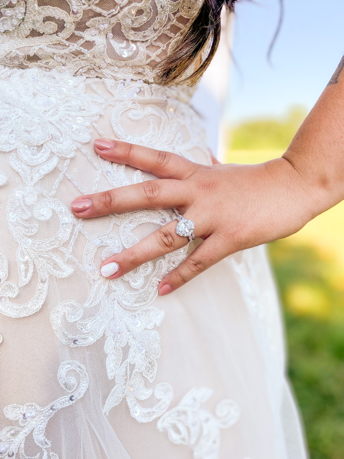 Close-up of a bride's engagement ring and freshly manicured nails resting on her lace wedding dress