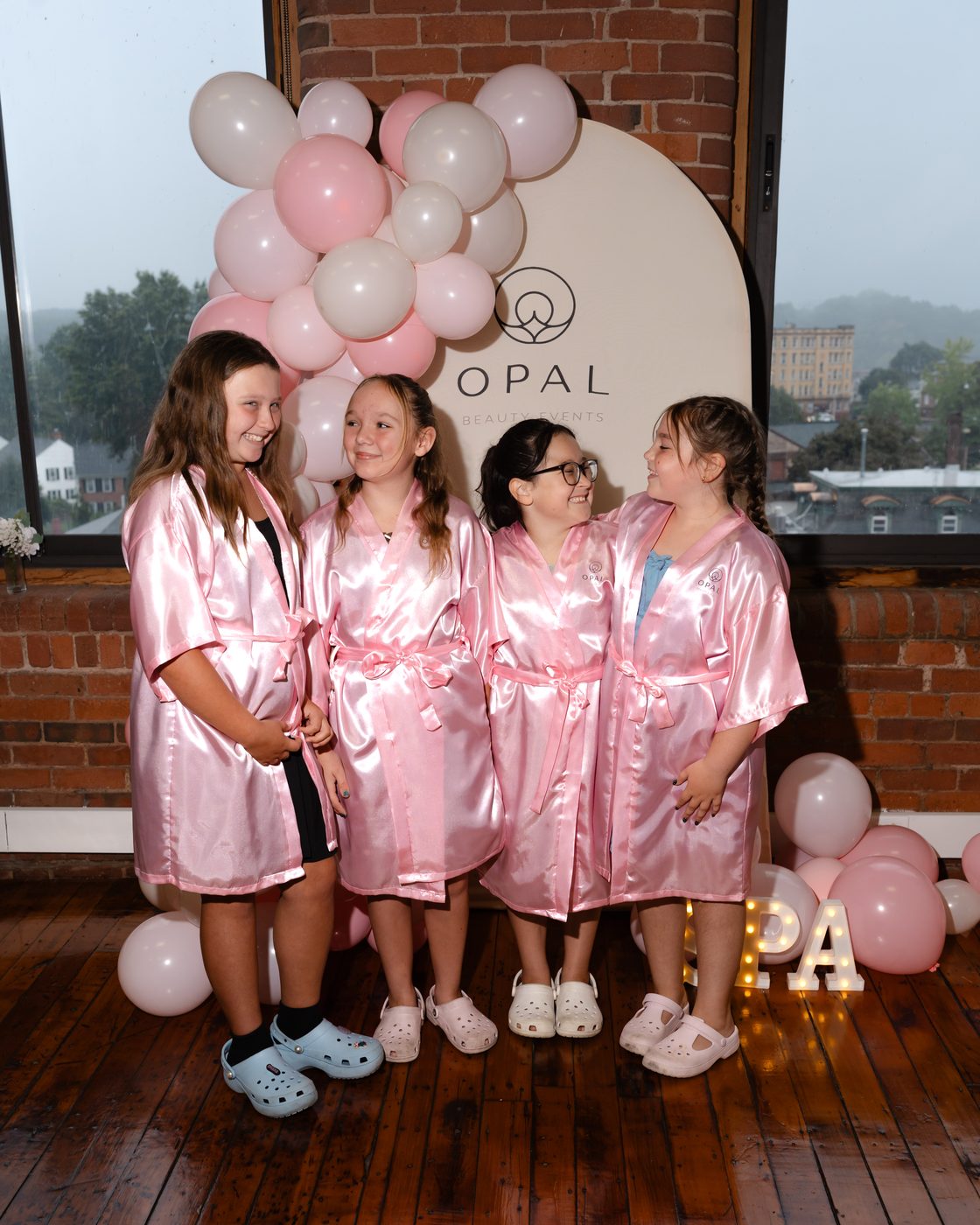 Four girls laughing together in front of the Opal Beauty Events balloon backdrop