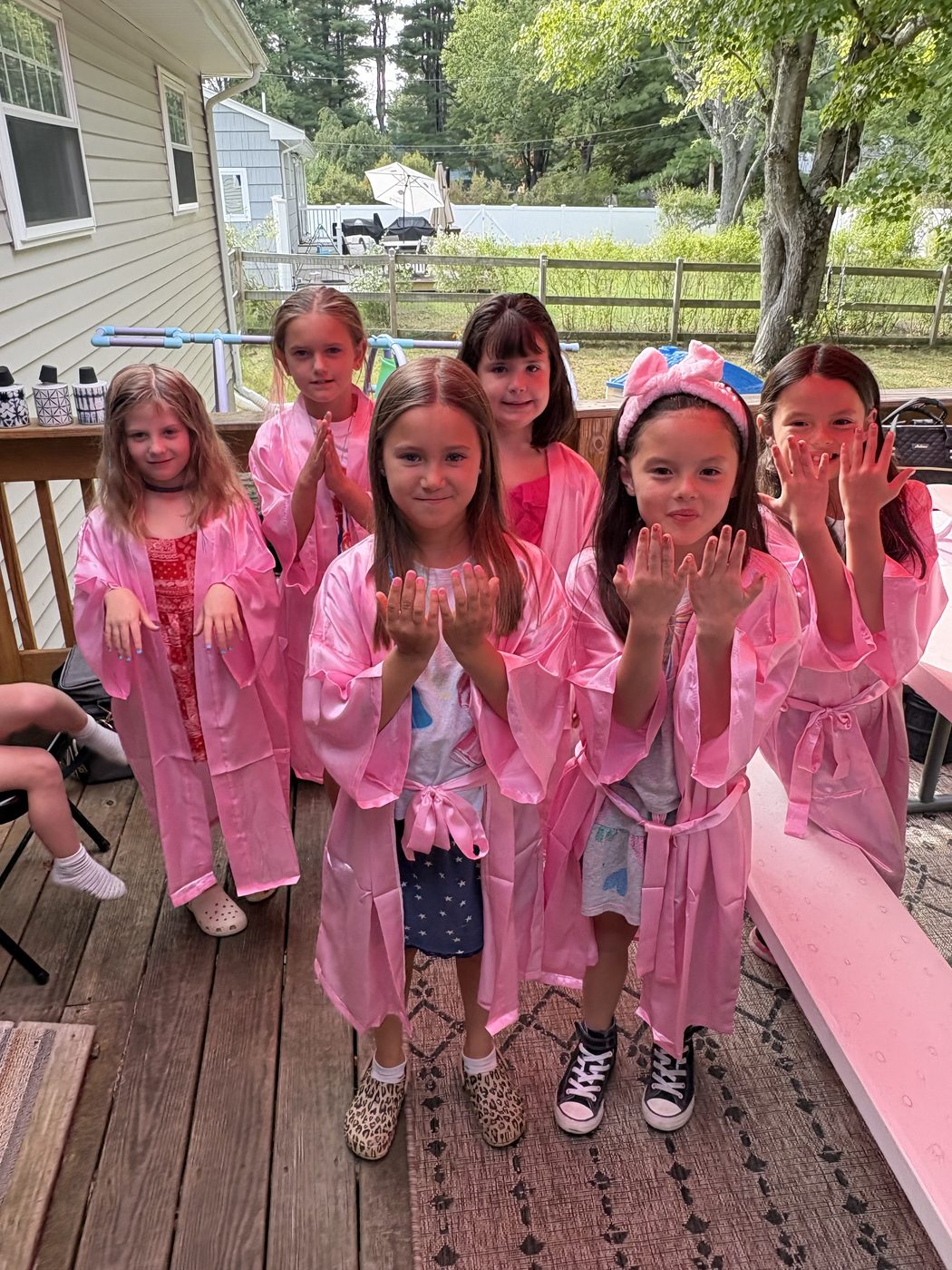A group of birthday guests in pink Opal robes posing together on the deck at a mobile spa party