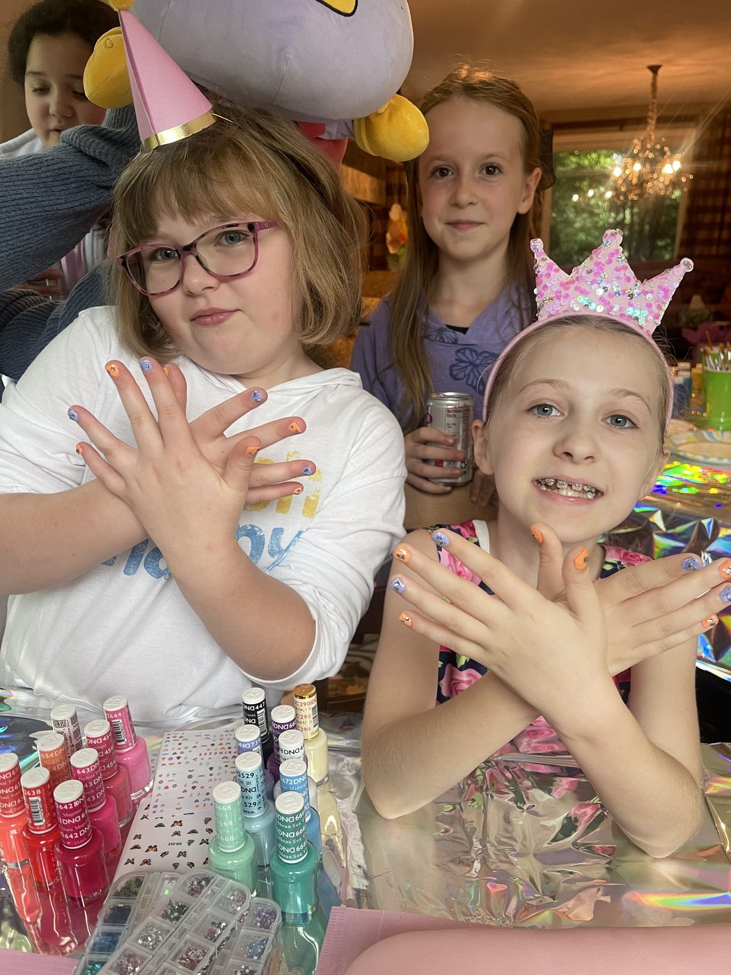 Three birthday party guests proudly showing off their colorful manicures at the nail polish station