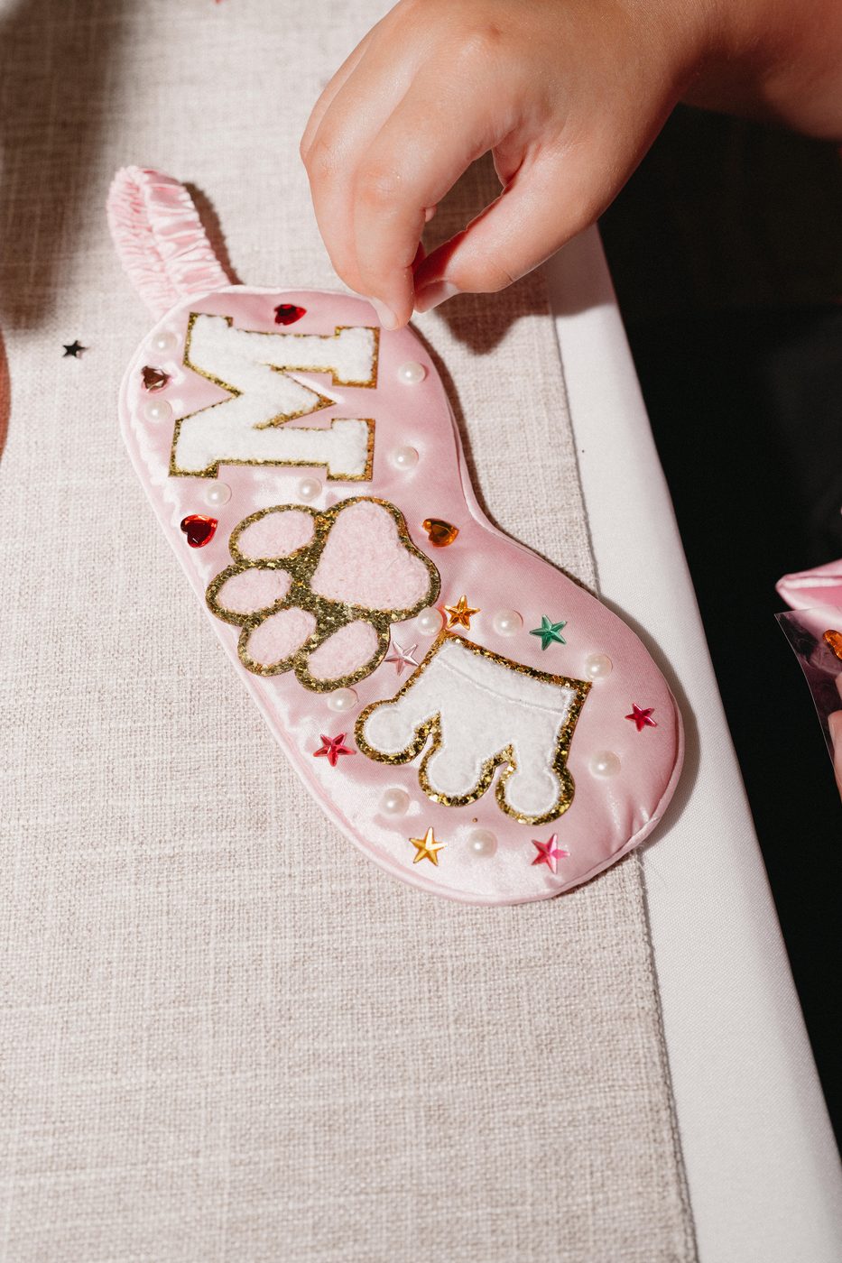 A personalized satin sleep mask decorated with rhinestones and a felt initial