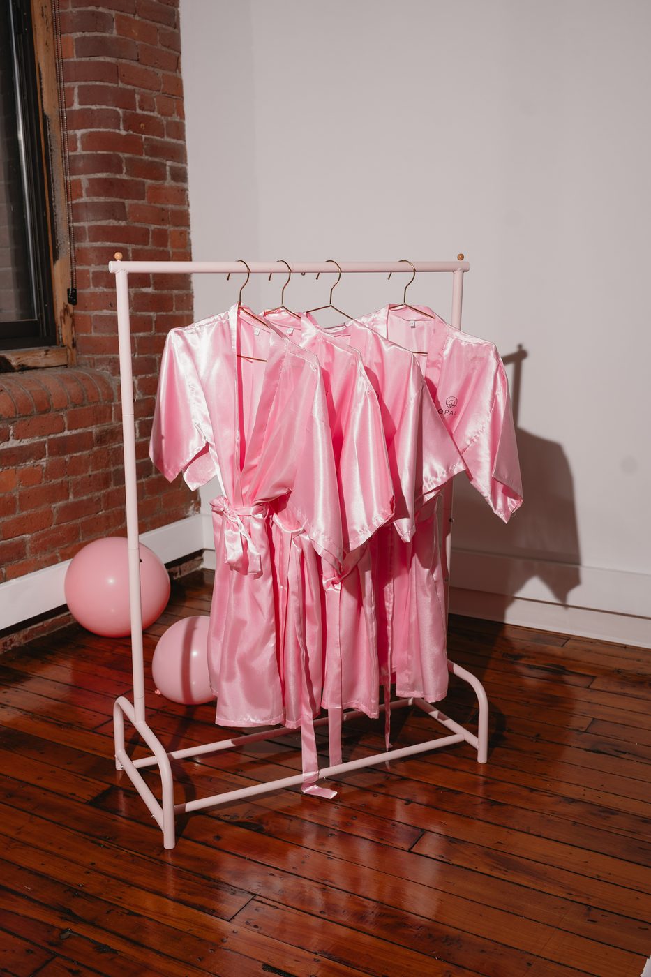 Pink satin Opal robes hanging ready for a kids spa birthday party in Massachusetts